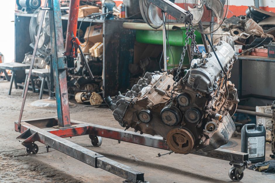 Close-up of a car engine hoisted in a mechanic's workshop, showcasing industrial tools.